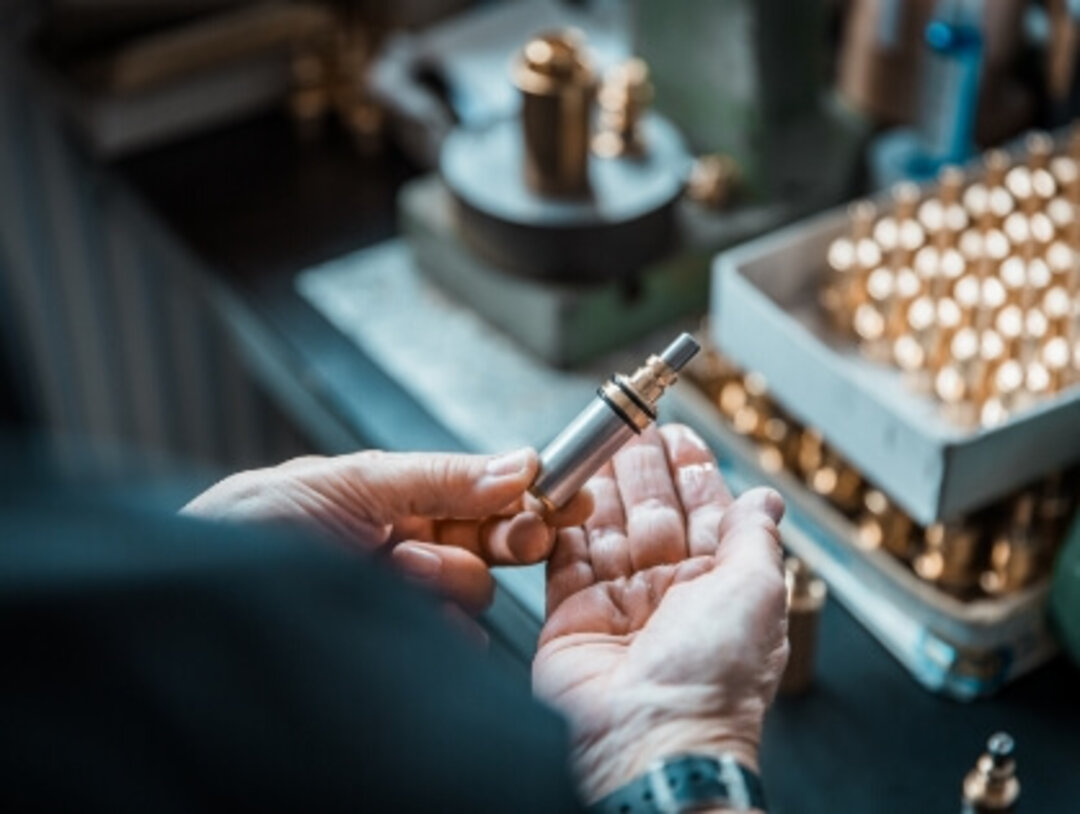 Hände eines Mitarbeiters halten ein Bauteil zur Sichtprüfung im Produktionsprozess.