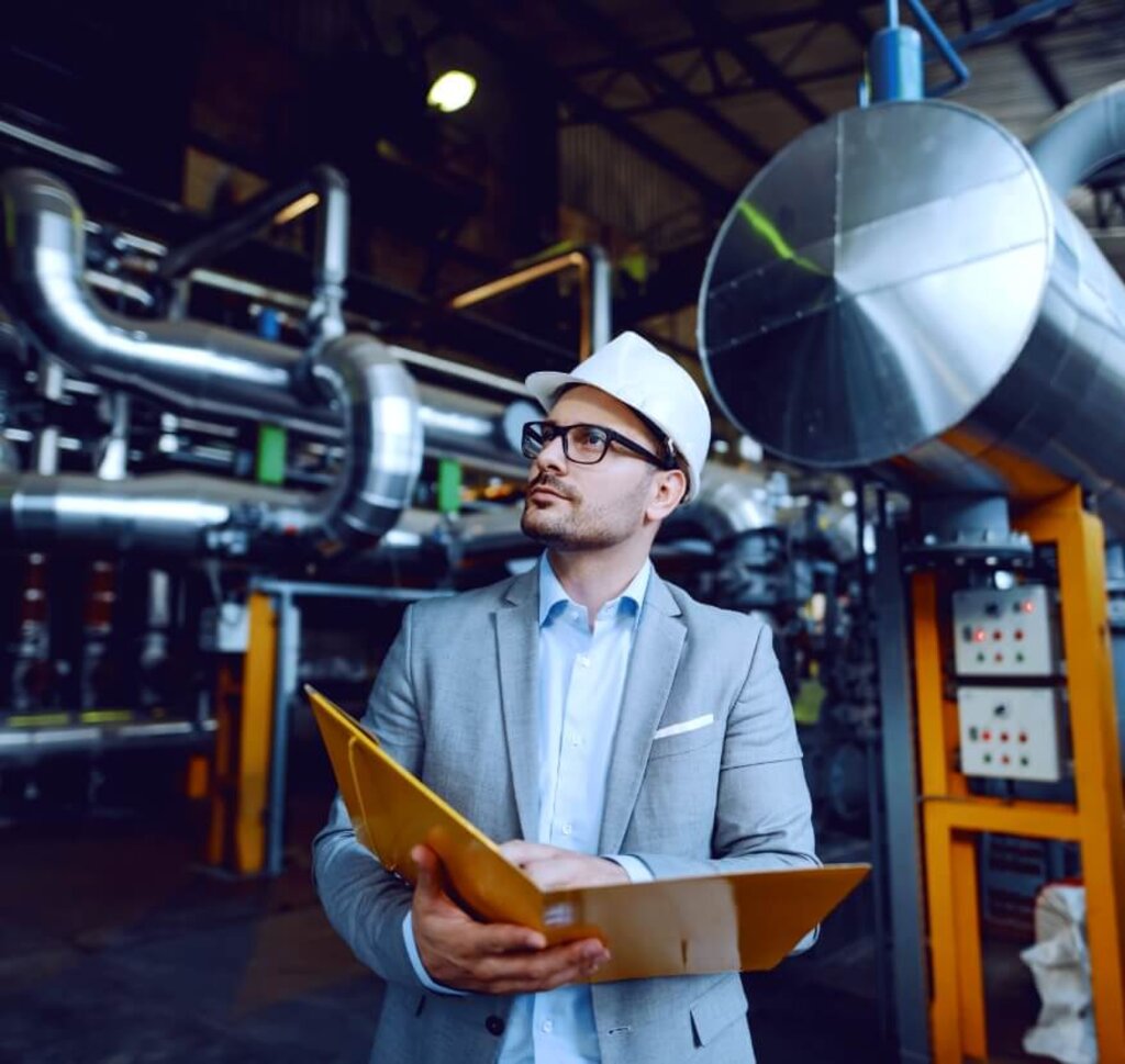Ingenieur mit Schutzhelm inspiziert eine industrielle Gasanlage und überprüft technische Dokumente vor komplexen Rohrleitungen.