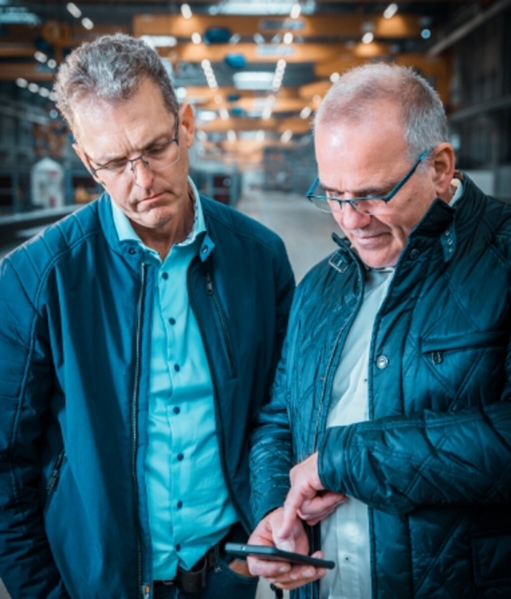 Zwei Fachberater prüfen gemeinsam technische Unterlagen in einer Industriehalle während eines Vor-Ort-Termins.