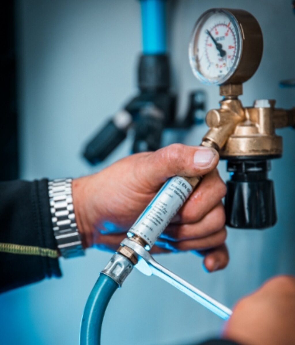 Hand eines Technikers, der eine Gasanlage mit Manometer und Anschlussleitung überprüft.