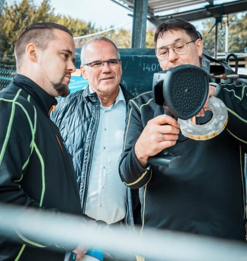 Drei Mitarbeiter stehen zusammen und prüfen ein tragbares Messgerät für Gas- oder Leitungsprüfung.